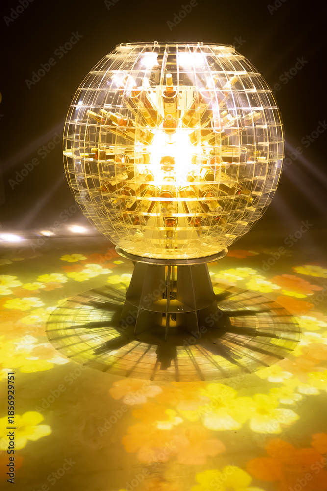 Obraz premium A glowing spherical transparent globe shaped lamp stands on a metal base radiates warm golden light in a dark room