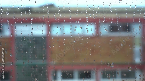 Raindrops dripping down a windowpane on a rainy day. Urban building is visible in the background, creating a moody and melancholic scene