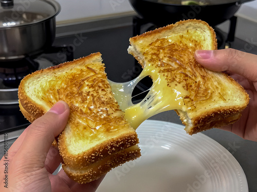 Hands pulling apart a freshly toasted grilled cheese sandwich with melted cheese stretching between slices in a kitchen setting