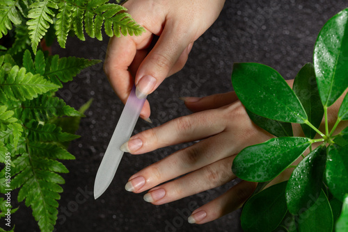 Foto Female hands doing a manicure with a glass nail file on natural long nails without coating, not painted