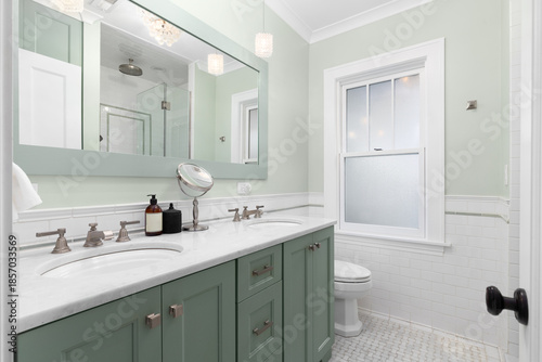 An elegant bathroom featuring a green double vanity and walls with a marble countertop, basketweave marble tile flooring, and glass pendant lights.