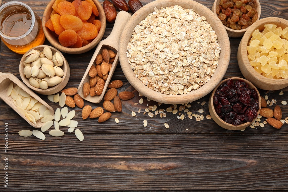 Fototapeta premium Making granola. Oat flakes, dried fruits and other ingredients on wooden table, flat lay. Space for text