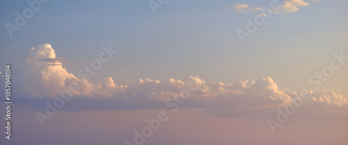 Soft pastel sky with fluffy cumulus clouds illuminated by warm evening light, calm atmospheric landscape, minimal background, peaceful mood, natural weather scene