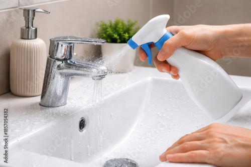 Cleaning bathroom sink with spray bottle and water droplets, hygiene maintenance in modern bathroom with faucet and soap dispenser, fresh and clean environment