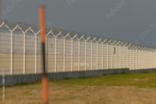 Tableau sur toile wide perimeter fence with razor coils conveying deterrence and exclusion, foregr