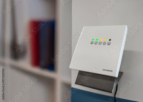 CO2 sensor with color coded indicator lights, visual warning system for monitoring air quality and ventilation needs. Carbon dioxide sensor with yellow warning lights in office, ventilate workspace.