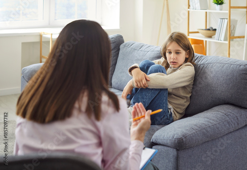 Tableau sur toile Female psychologist doctor talking with her child boy patient sitting on sofa during therapy session