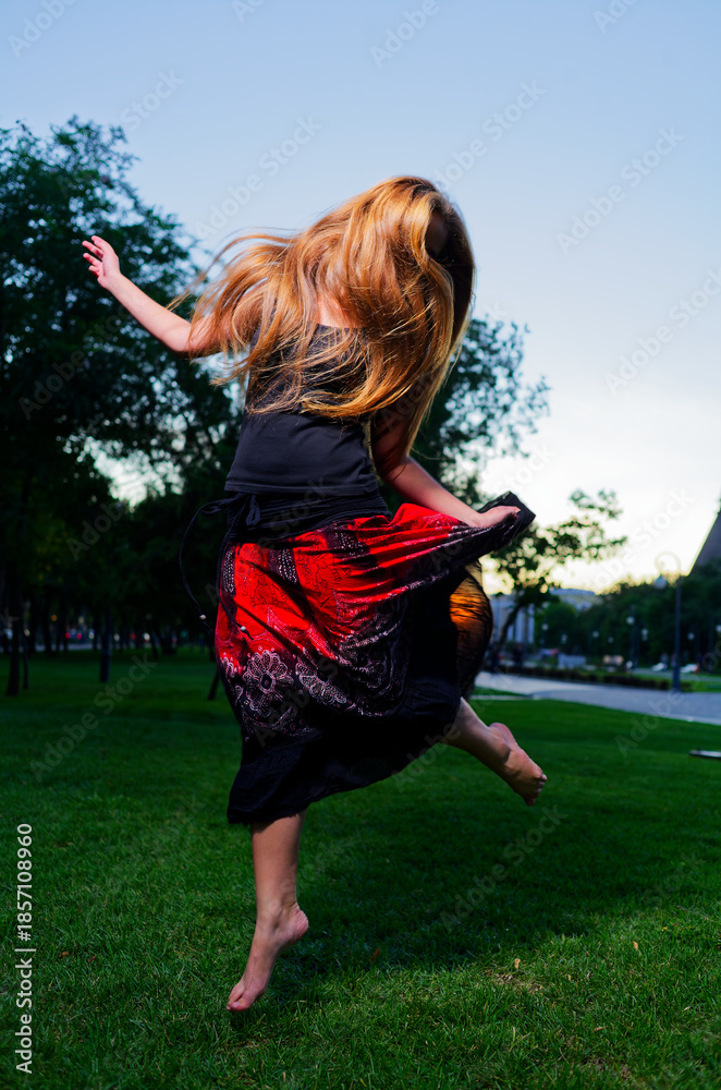 custom made wallpaper toronto digitalJoyful Movement: Young Woman Dancing with Long Hair Flowing Outside in Vibrant Dress Captured in Park Setting at Twilight