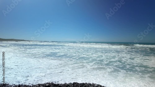 Strong ocean surf breaking on pebble beach in sunlight