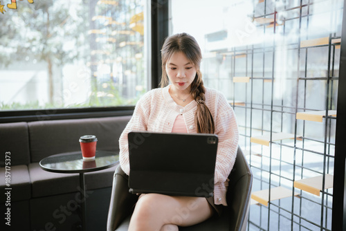 Free Download A young woman works on a laptop while sitting in a modern café, enjoying a quiet moment with coffee, reflecting a freelance lifestyle, remote work, and productivity in a cozy space. - GFXLoad
