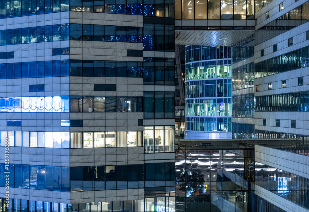 Obraz premium Tall buildings show bright windows at night. Some offices are active with lights on, while others are dark. The design features glass and concrete structures.