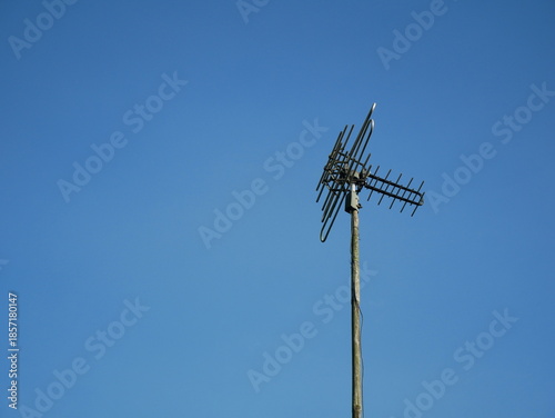 A television antenna mounted on a metal pole stands against a clear blue sky. 