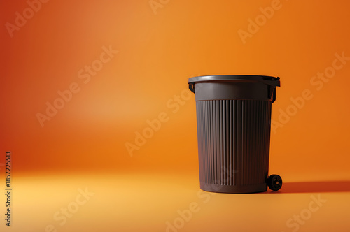 A small dark miniature trash can or recycling bin stands against a vibrant orange background in a minimalist studio setting