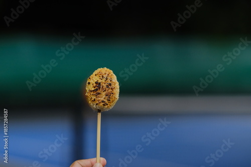Rice balls are shaped into spheres, skewered, and grilled over a fire.