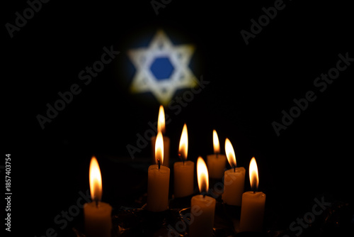 Schilderij op canvas Lit candles shine in front of a bright blue Star of David on a black background,