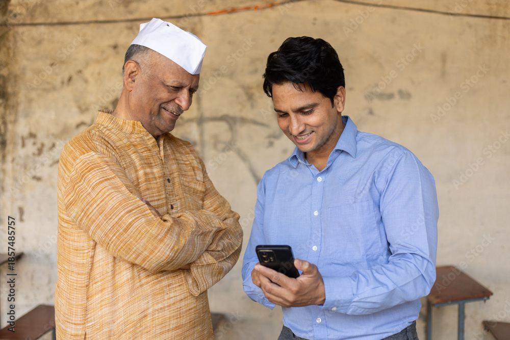 Fototapeta premium Young indian bank person or finance adviser showing information to senior farmer on smart phone. Government scheme, Agriculture or business loan, Rural india, Support and assistance.
