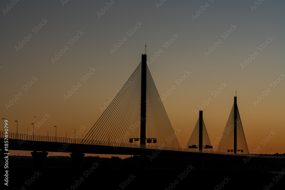 Obraz premium Mersey Gateway Bridge silhouetted against a warm sunrise sky above the River Mersey at low tide