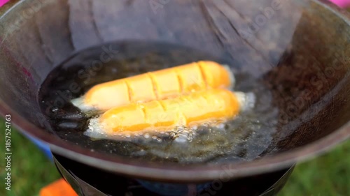 Frying sausages in a pan filled with hot oil during outdoor cooking activities.