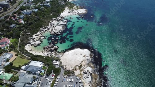 Aerial view of Simon's Town coastline near Boulders Beach, Cape Town, South Africa, featuring luxury residential houses, coastal road, turquoise ocean and mountains on a sunny summer day in Western Ca
