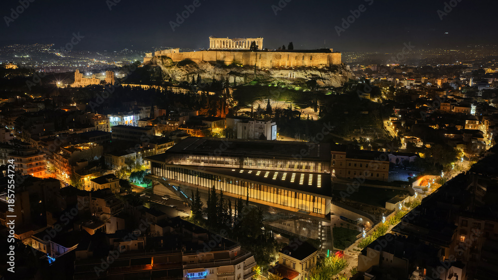 Fototapeta premium Aerial drone night shot of iconic new modern Acropolis museum, Acropolis hill and the Parthenon at the background, Athens historic centre, Attica, Greece