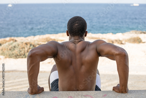 Man doing push-ups on bench outdoors. Athletic man performing incline push-up exercise on a concrete bench during outdoor workout by the sea.
