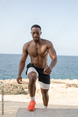 Athletic man training legs with step-up exercise outdoors. 
Fit man performing step-up exercise on a concrete bench during outdoor fitness training by the sea.