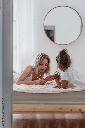 Mother and daughter lying on bed drawing