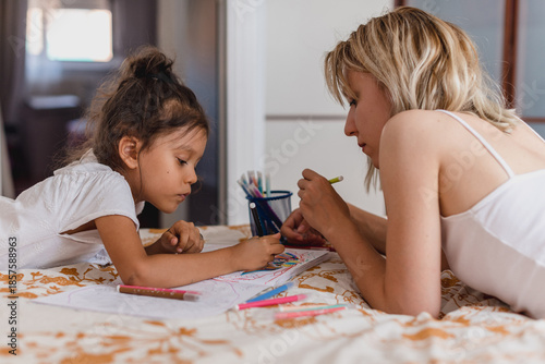 Mother and daughter lying on bed drawing