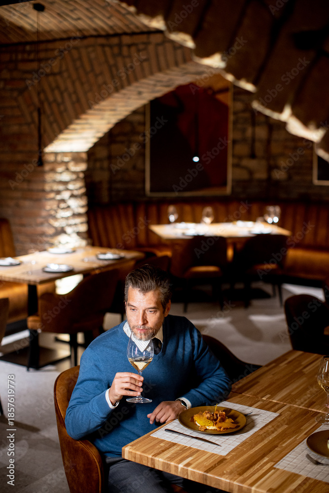 © BGStock72 - Man sitting at table in restaurant with meal and drink during evening