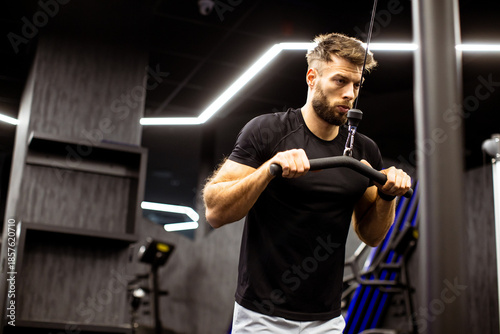 Bild auf Leinwand Man using cable machine to train upper body strength in modern gym setting