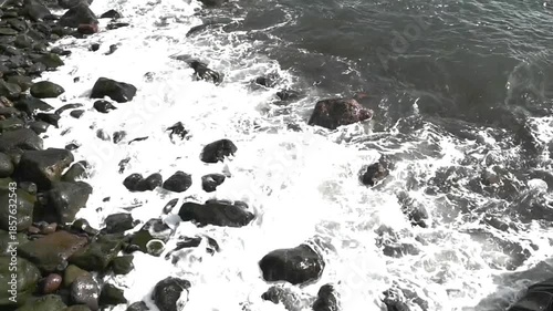 waves of the Atlantic Ocean splashing on grey volcanic rocks and pebbles on a beach