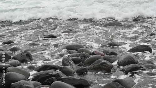 waves of the Atlantic Ocean splashing on grey volcanic rocks and pebbles on a beach