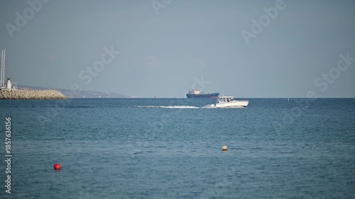 Small motorboat cruising on calm sea with cargo ship in the background, The entrance of the new Limassol Marina