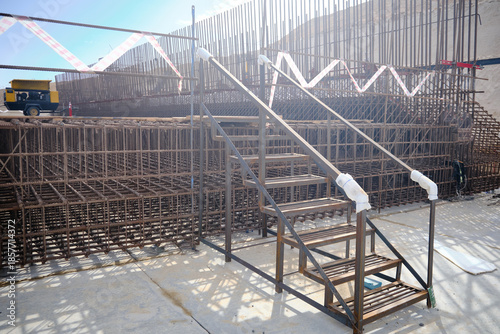 Temporary metal staircase installed at active construction site, providing safe access over steel reinforcement and concrete formwork. Construction infrastructure, site safety measures