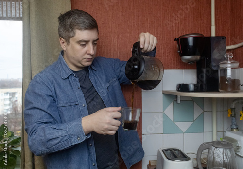 Man preparing fresh coffee at home using an electric coffee maker. Casual morning routine in a cozy kitchen, everyday lifestyle, simple domestic moment, authentic home brewing scene.