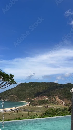 Gorgeous tropical scenery featuring a picturesque sandy beach, vibrant green hills, and a tranquil infinity pool overlooking the breathtaking vista on a sunny day with a cloudless sky