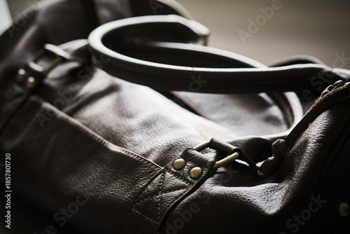Close-up view of dark leather bag focusing on handle, strap attachment, and metal hardware. Natural leather texture, stitching, craftsmanship, premium materials