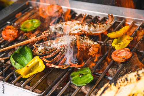 Grilled spiny lobsters with flames, pineapple and vegetables on an open outdoor grill