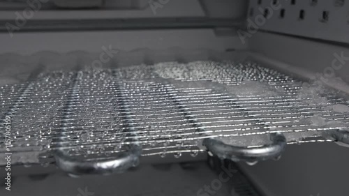 Freezer defrosting process showing melting ice and water droplets on wire shelf, gradual removal of frost buildup in kitchen appliance