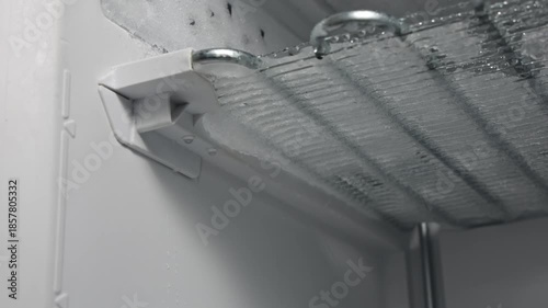 Ice melting and dripping from freezer shelf in a refrigerator, showcasing the defrosting process with visible water droplets accumulating