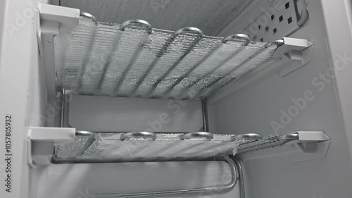 Ice melting and dripping from freezer shelves, showcasing gradual defrosting process with visible water droplets forming and falling down