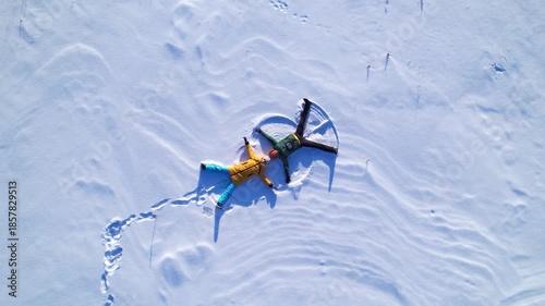 Top view aerial shot of a man and woman lying on fresh snow and making snow angel shapes. Winter outdoor activity, happiness, freedom and seasonal lifestyle concept with copy space.