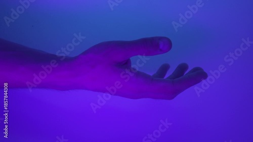 A male hand in a glowing neon liquid inside a laboratory