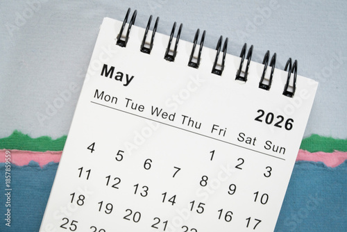 May 2026 - small spiral desktop calendar against art paper abstract, time and business concept