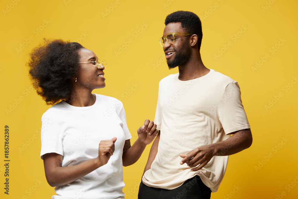 Obraz premium Happy young couple enjoying a joyful moment together against a vibrant yellow background in casual clothing, representing love and connection