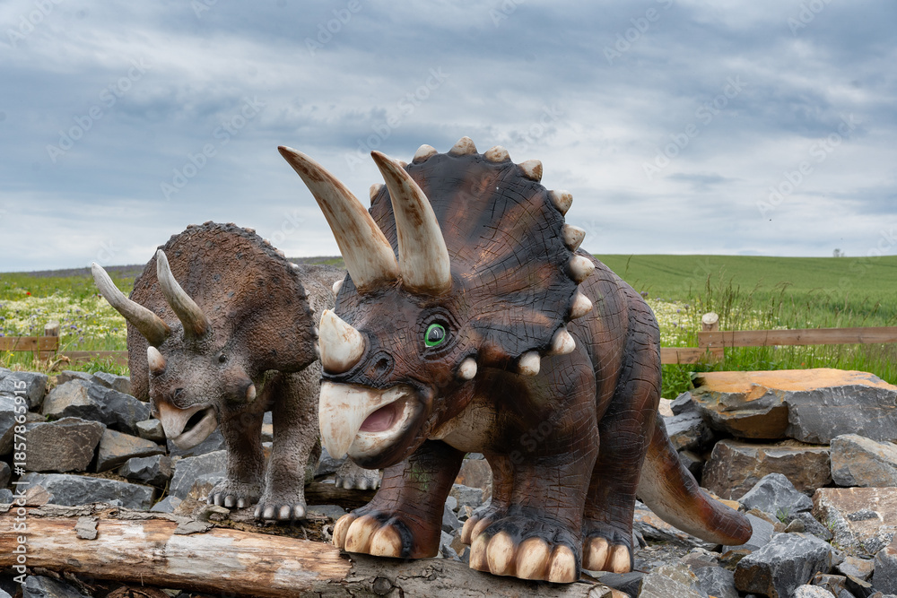 Fototapeta premium Life-size triceratops dinosaur sculptures in a family-friendly outdoor park. Realistic prehistoric animals displayed in nature, educational dinosaur attraction for children
