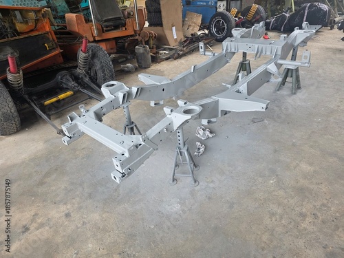 Fotografie Freshly painted vehicle chassis frame supported on jack stands in a garage, surrounded by tools and parts during restoration or assembly