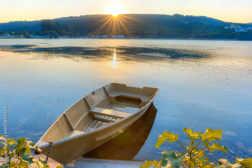Obraz premium A boat on the shore of Lake Abrau-Dyurso in the rays of the rising sun. A beautiful summer sunrise on the lakeshore.