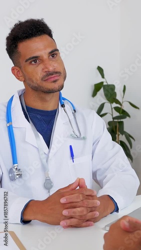 Vertical HD video of young male doctor talking with patient at medical consultation. Professional explaining medical information clearly. Healthcare and communication concept. 