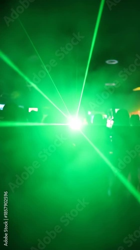 Green laser light show in a dark room with people silhouettes dancing.